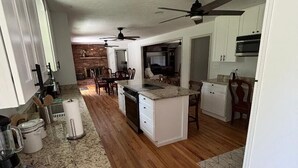 A kitchen with granite countertops, white cabinets, wooden flooring, ceiling fans, and a brick wall in the background. - 4 BR/3 BA-Great for extended stays- Close to Savannah River Site & Masters Golf (Aiken)