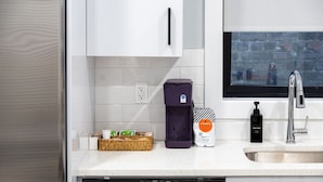 Uma cozinha moderna com armários brancos, lava-louças de aço inoxidável, máquina de café e um frasco de detergente.