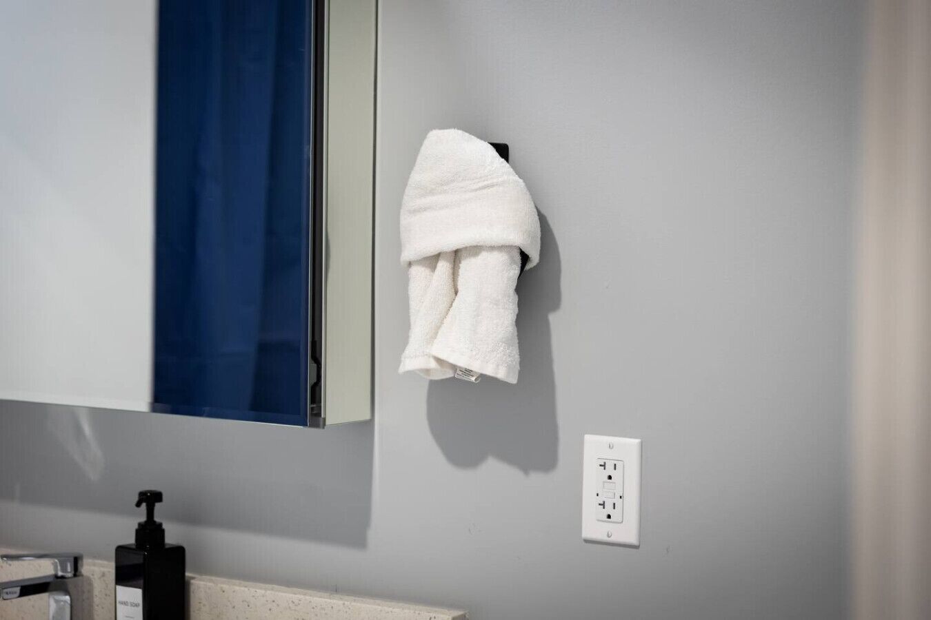 Un baño con una toalla blanca colgada en un gancho, una cortina de ducha azul y un dispensador de jabón para manos sobre la encimera.