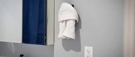 Un baño con una toalla blanca colgada en un gancho, una cortina de ducha azul y un dispensador de jabón para manos sobre la encimera.