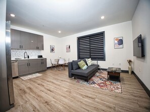 A modern living room with a grey sofa, a coffee table, and a dining area with a white table and chairs. - Prime Location-Free Parking-20 Min to Times Square (West New York)