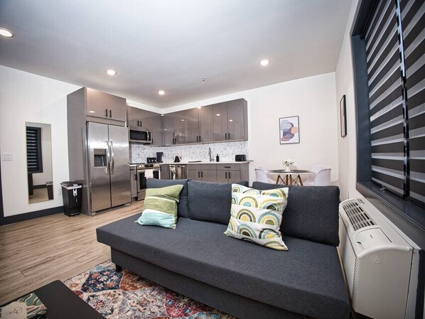 A modern apartment with a grey sofa, kitchen, and dining area. - Prime Location-Free Parking-20 Min to Times Square (West New York)