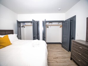 A bedroom with a bed, a wooden dresser, and a wardrobe with open doors. - Prime Location-Free Parking-20 Min to Times Square (West New York)