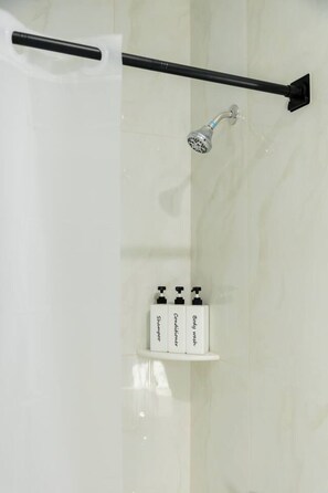 A bathroom with a shower, a towel rack, and three toiletries on a shelf. - Modern 1BR w/ Indoor Parking • Quick Access to NYC (West New York)