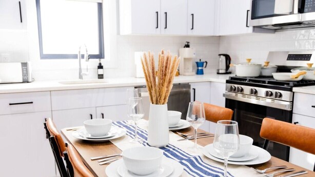 Una cocina moderna con armarios blancos, electrodomésticos de acero inoxidable y una zona de comedor lista para una comida.