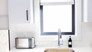 Una cocina con un tostador de acero inoxidable, un lavamanos con grifo y una ventana sobre el lavamanos.