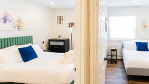A hotel room with two beds, a green headboard, a bedside table with a lamp, and artwork on the wall.