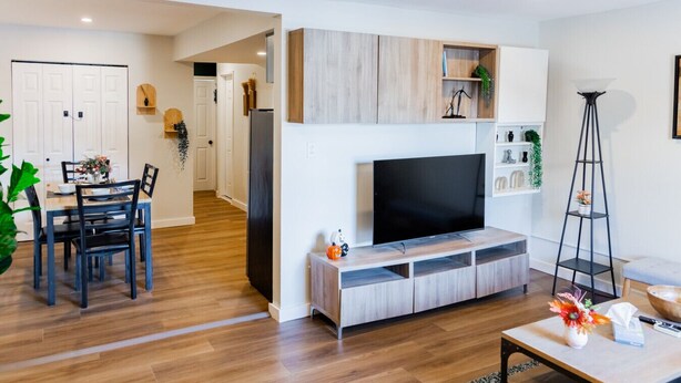 A modern living room with a TV, wooden cabinets, a dining area with chairs, and a floor lamp.