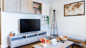 A modern living room with a flat-screen TV, wooden cabinets, a tall floor lamp, a bowl on a coffee table, and a world map on the wall.