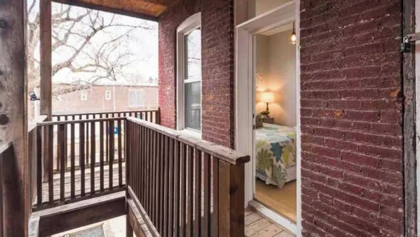 Een houten balkon met uitzicht op een bakstenen gebouw en een boom.