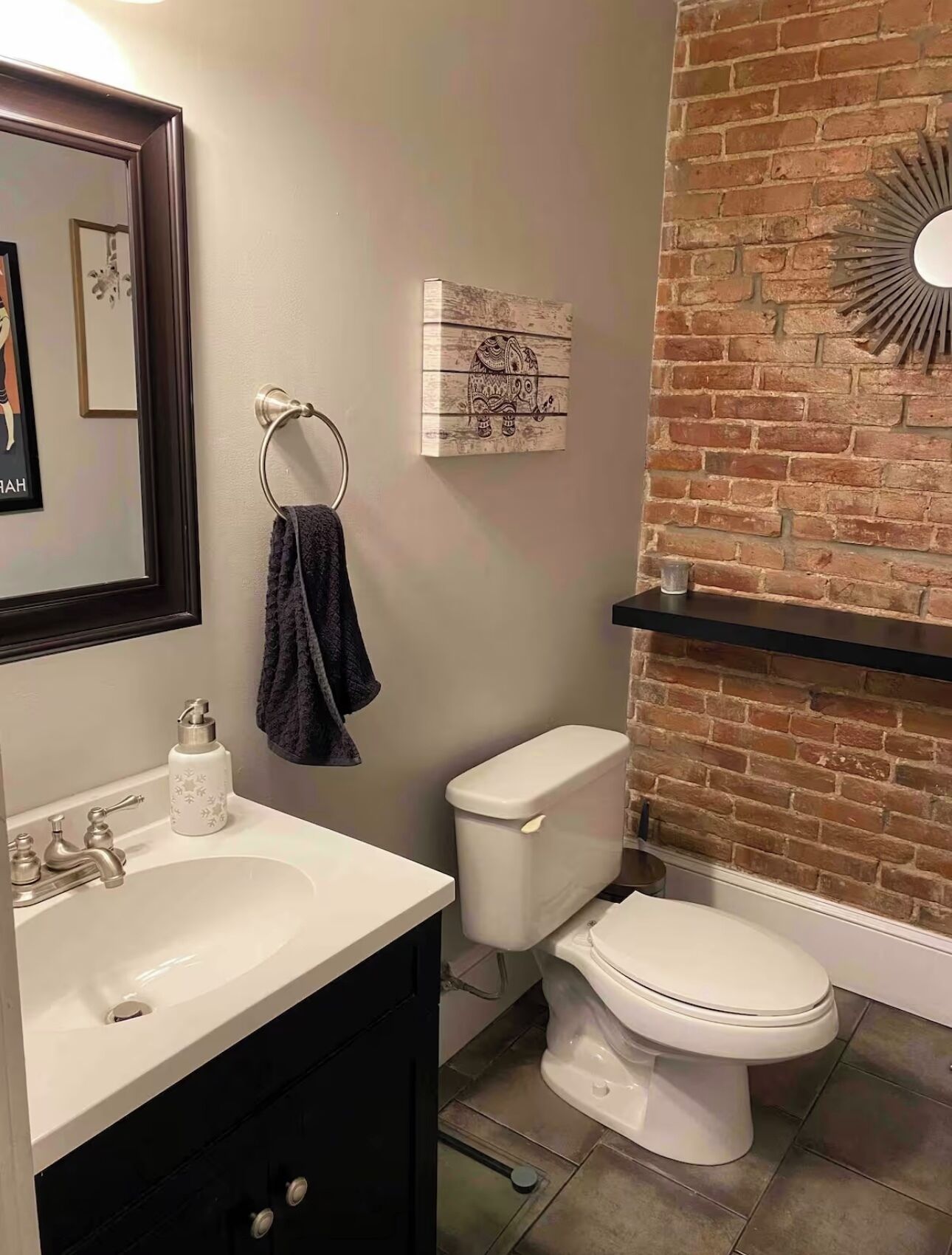 A bathroom with a white sink, a toilet, and a mirror. There is a towel rack with a towel hanging on it. A decorative piece with an elephant design is on the wall.