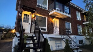 A two-story residential building with a front porch, a staircase, and a small garden area.