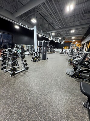 Ett gym med olika typer av träningsutrustning, inklusive styrketräningsmaskiner och hantlar.