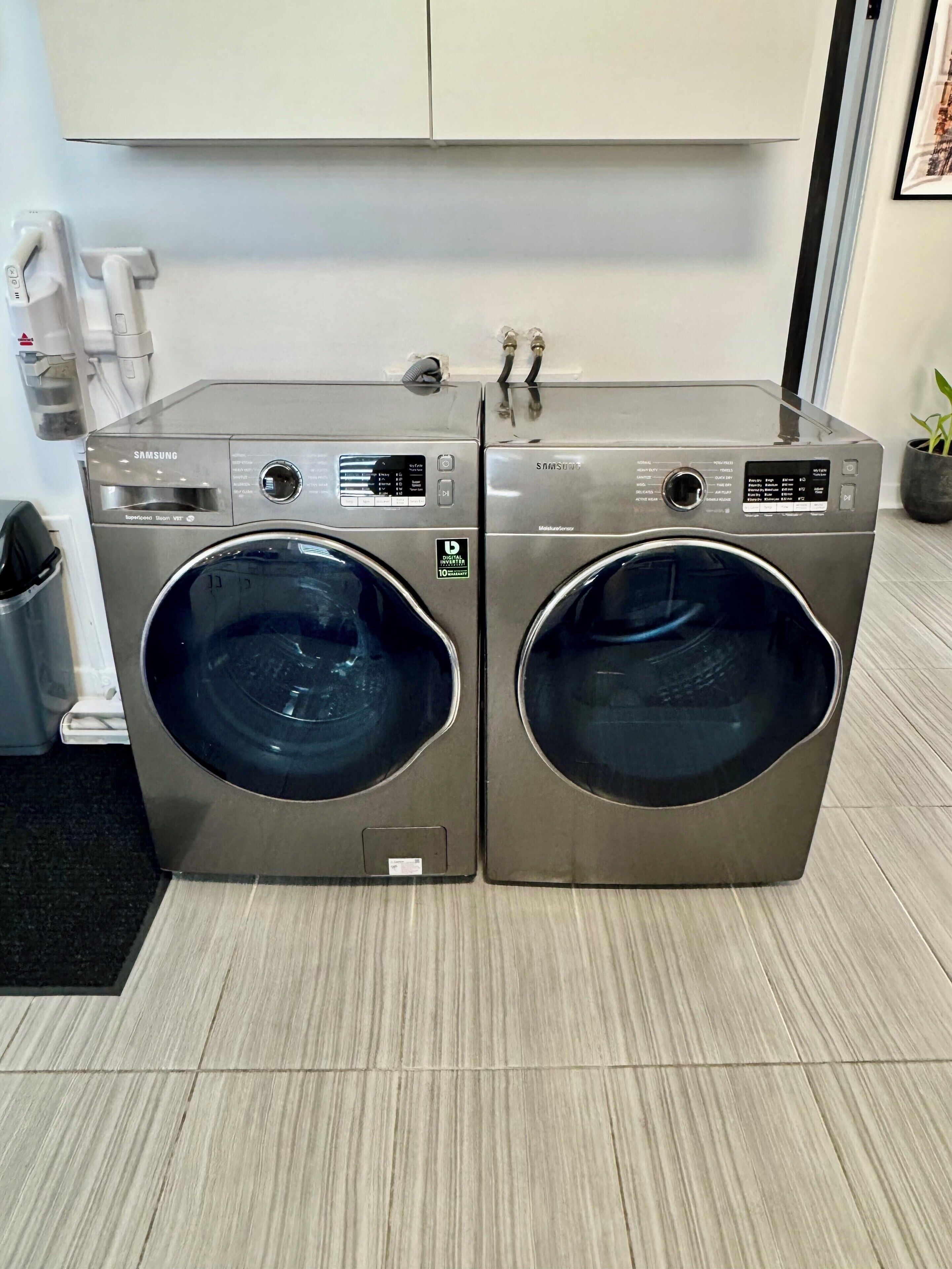Two Samsung front-loading washing machines in a modern kitchen with a tiled floor and a white cabinet above.