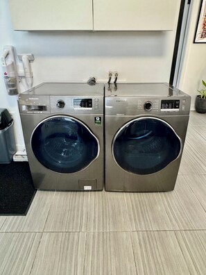 Dos lavadoras Samsung de carga frontal en una cocina moderna con piso de baldosas y un gabinete blanco arriba.