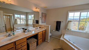 A modern bathroom with dual sinks, a large mirror, a bathtub, and a view of the outdoors through a window. - Charming 4-bedroom house in Woodstock perfect for your getaway (Woodstock)