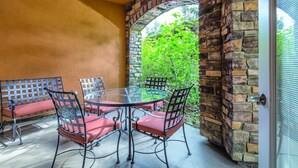 Une terrasse avec une table en verre et des chaises en métal, entourée d’un mur de pierre et offrant une vue sur la verdure.