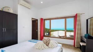 A hotel room with a bed, a desk, and a large window with a view of the sea.