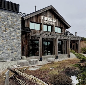 A spa village named Thermea with stone walls, wooden architecture, and large windows.