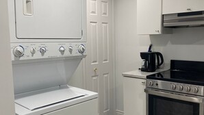 Cocina compacta con lavadora y secadora integradas, estufa de acero inoxidable y armarios blancos.