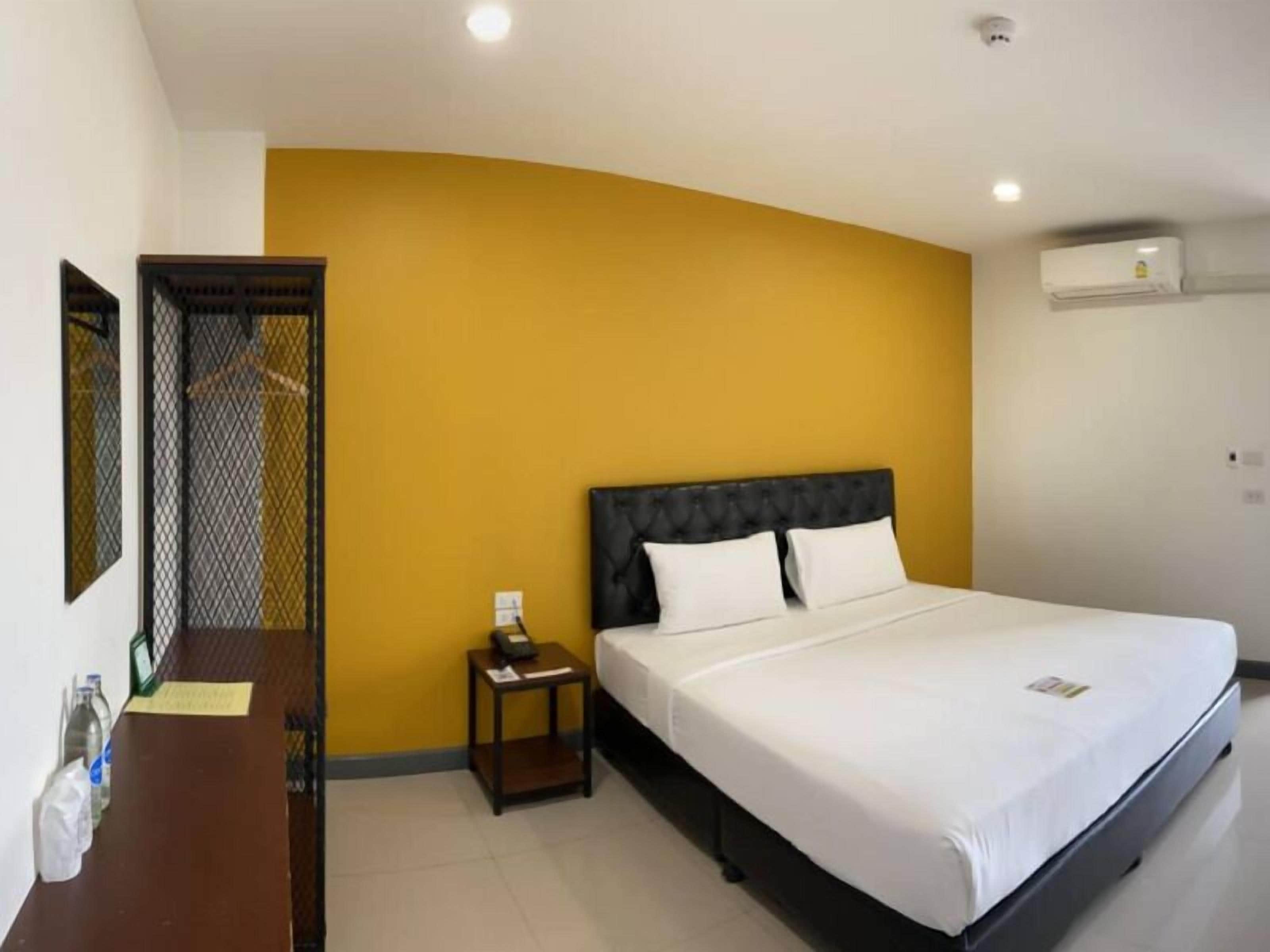 Quarto de hotel com uma cama, mesa de cabeceira, escrivaninha e espelho.