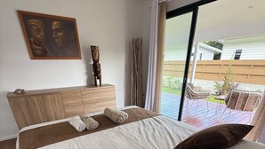 Une chambre d’hôtel avec un grand lit, une tête de lit en bois, un tableau et une vue sur la terrasse extérieure.