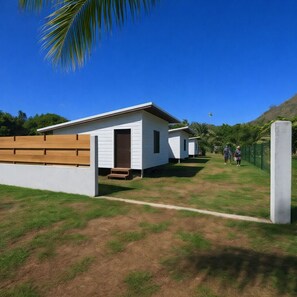 A row of white mobile homes with a wooden deck in front, set against a clear blue sky.