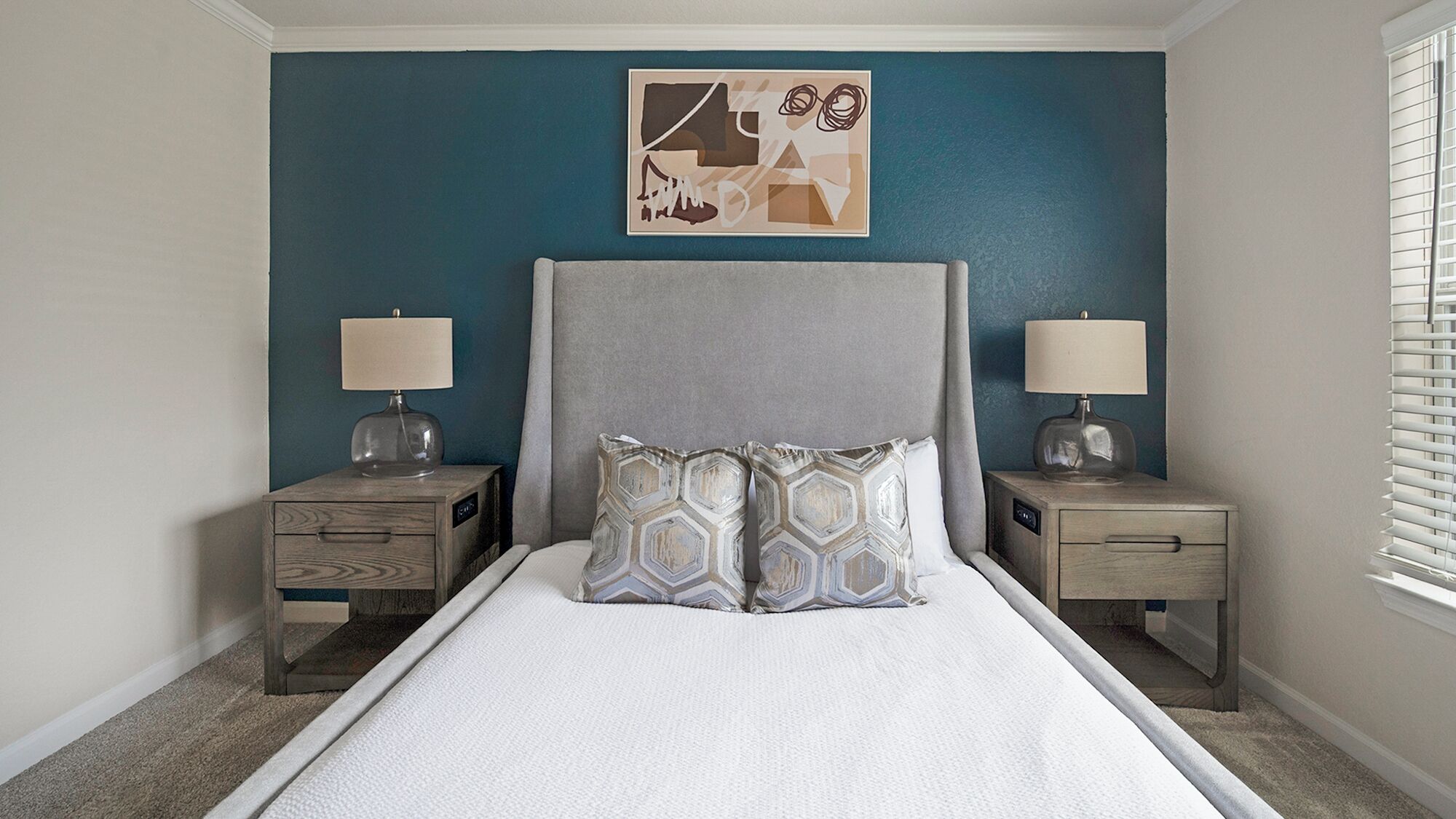 A bedroom with a bed, two nightstands, a wall art piece, and a window with blinds.