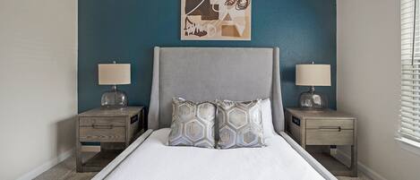A bedroom with a bed, two nightstands, a wall art piece, and a window with blinds.