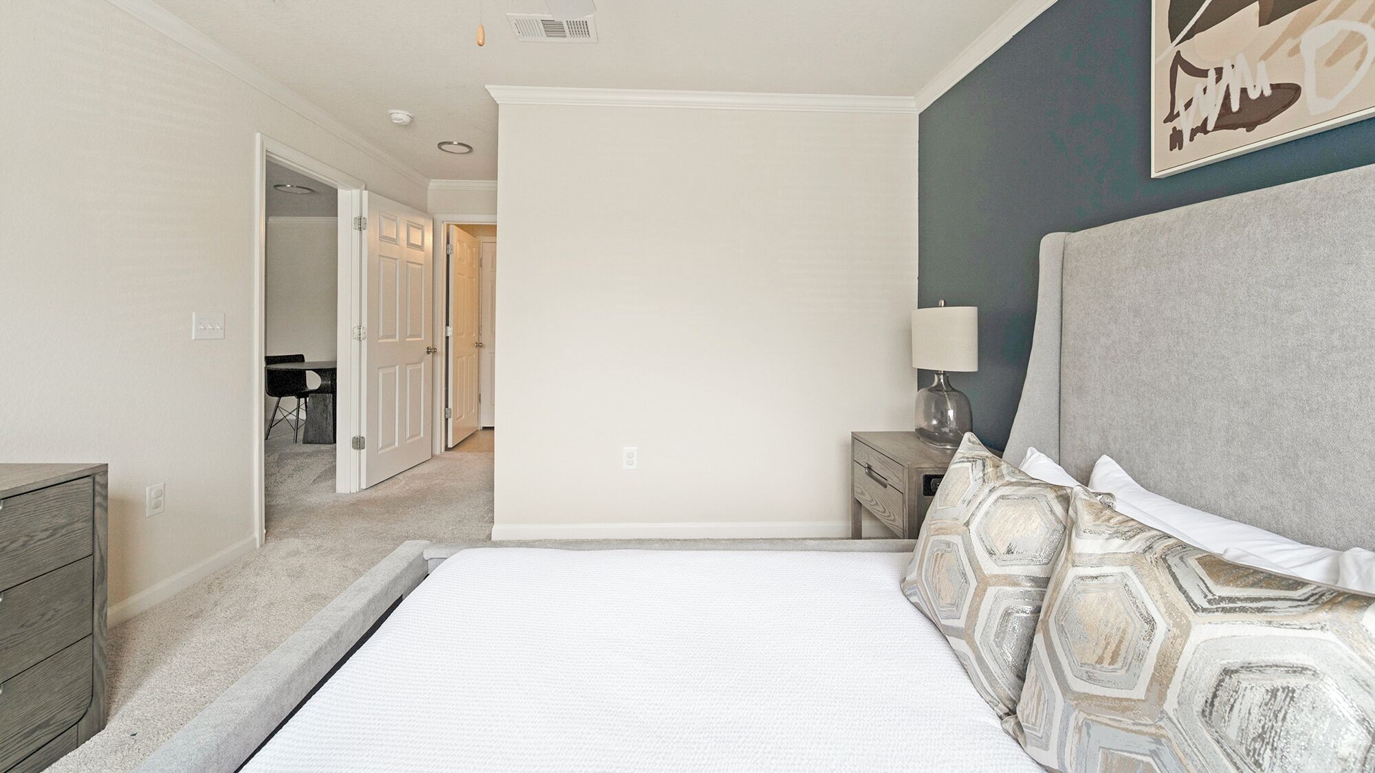 A bedroom with a large bed, a nightstand, a lamp, and a wall with a geometric pattern.