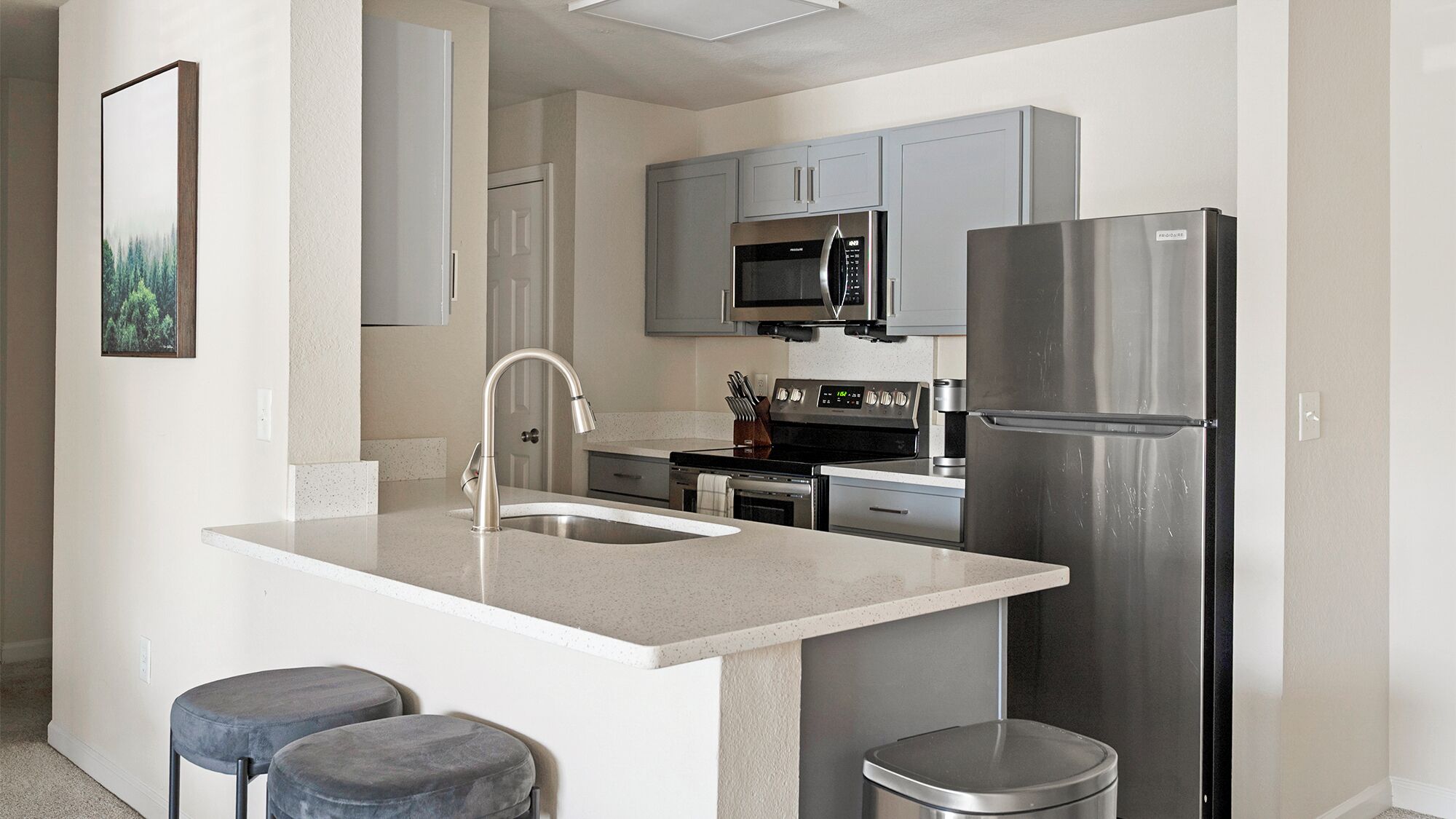 A modern kitchen with a central island, stainless steel appliances, and grey cabinetry.