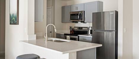 A modern kitchen with a central island, stainless steel appliances, and grey cabinetry.