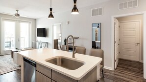A modern kitchen with a large island, a dishwasher, and a built-in oven. There are pendant lights above the island and a ceiling fan. - Landing Near UNC Charlotte (Charlotte)
