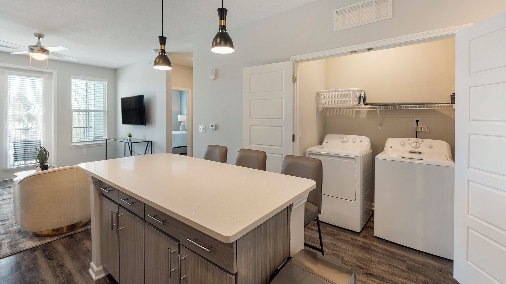 A modern kitchen with a central island, two wall-mounted pendant lights, a built-in washer and dryer, and a dining area with a table and chairs.