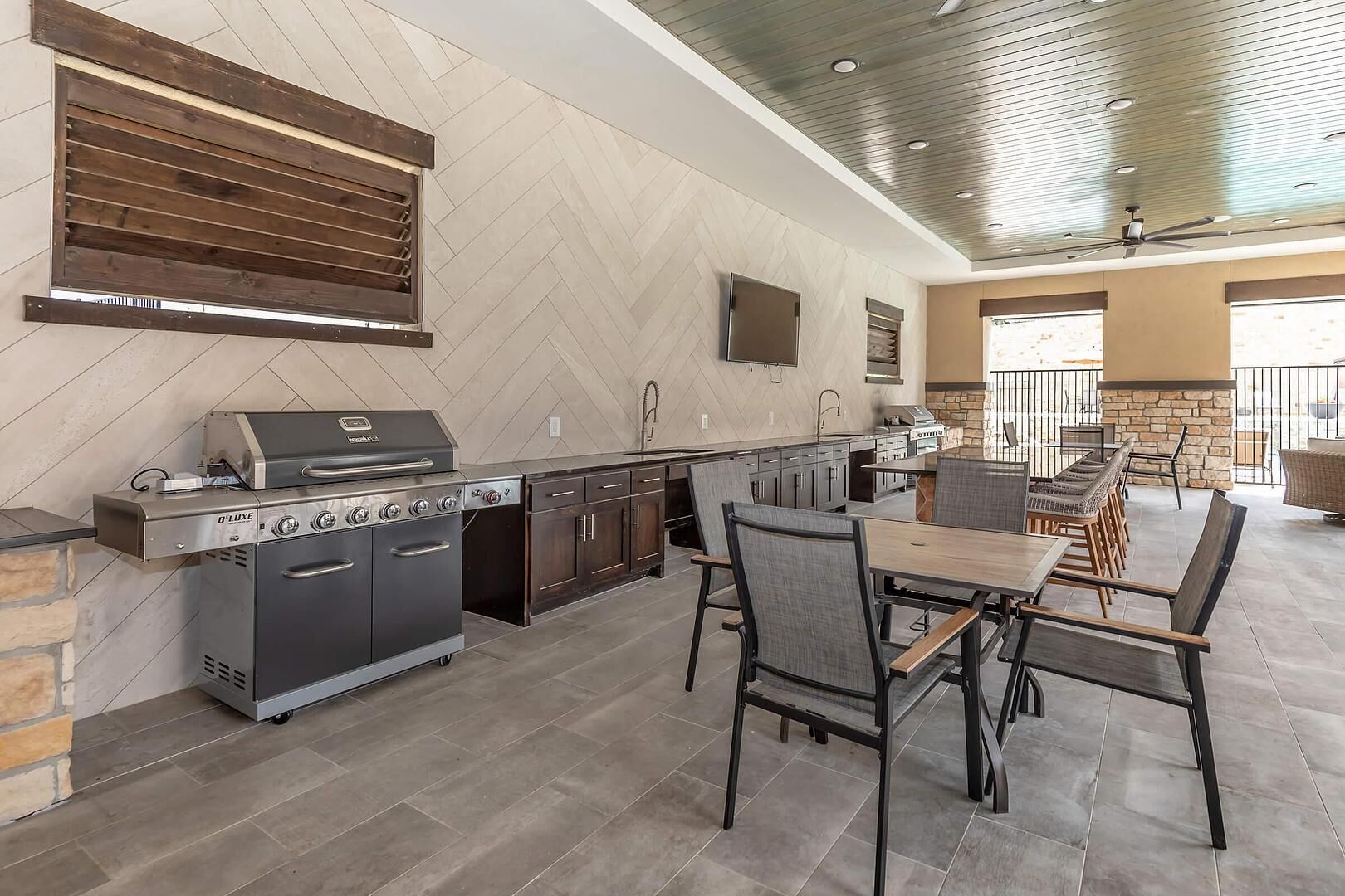 An outdoor kitchen with a built-in grill, dining area with chairs, and a stone accent wall.