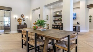 Un'ampia sala da pranzo con tavolo in legno e sedie in vimini, una pianta in vaso e una libreria sullo sfondo.