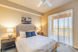 A bedroom with a large bed, two bedside tables with lamps, a ceiling fan, and a view through a sliding glass door.