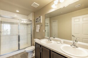 A bathroom with a glass-enclosed shower, two sinks, a toilet, and a large mirror.