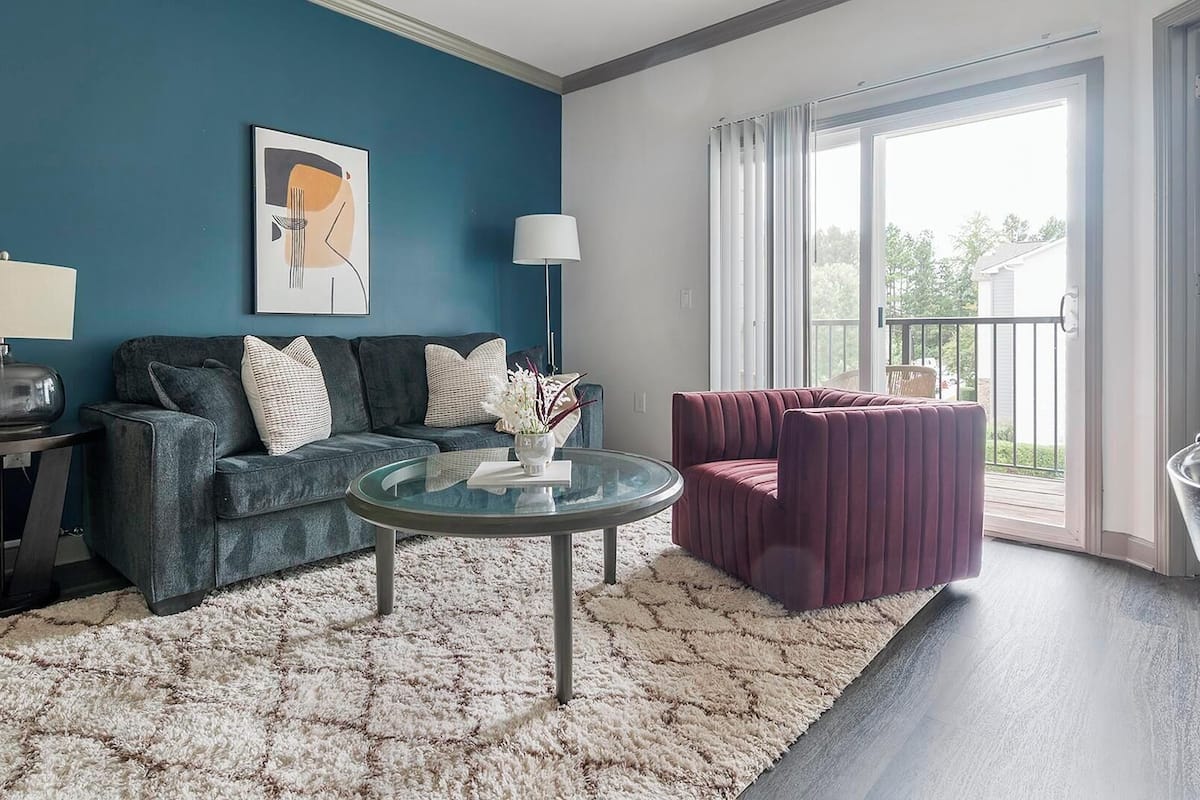 A living room with a blue wall, a grey sofa, a glass coffee table, and a purple armchair.