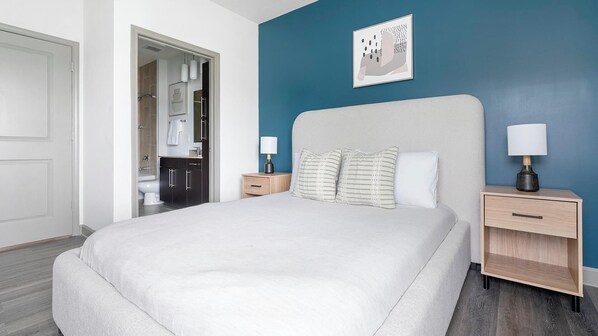 A bedroom with a bed, nightstands, a dresser, and a bathroom visible through an open door.
