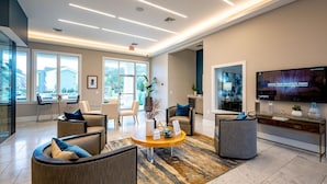 A modern hotel lobby with a large TV, comfortable seating, and a view of the outdoors. - Landing Apartments - North Charlotte (Charlotte)