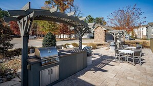 An outdoor patio with a grill, seating area, and a pergola structure. - Landing Apartments - North Charlotte (Charlotte)