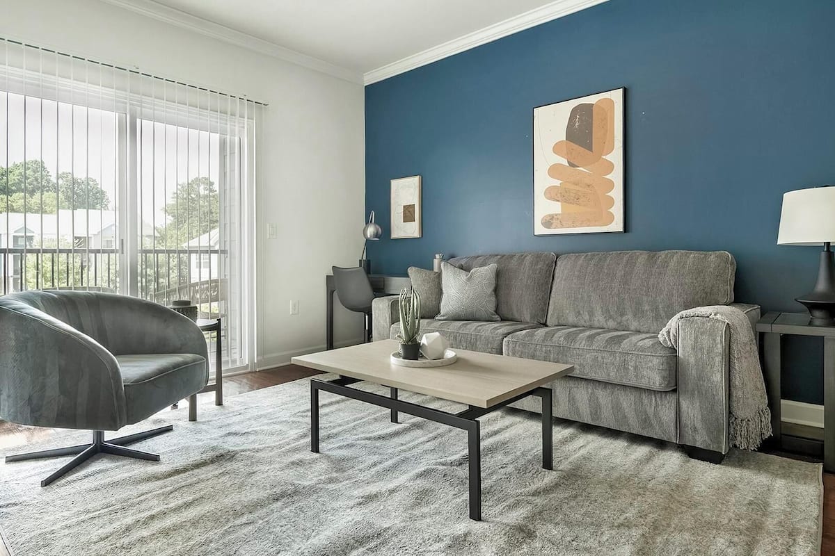 A living room with a grey sofa, a black chair, a coffee table, and a blue accent wall.