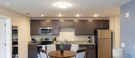 Una cocina moderna con armarios oscuros, electrodomésticos de acero inoxidable y una zona de comedor con una mesa redonda y sillas.