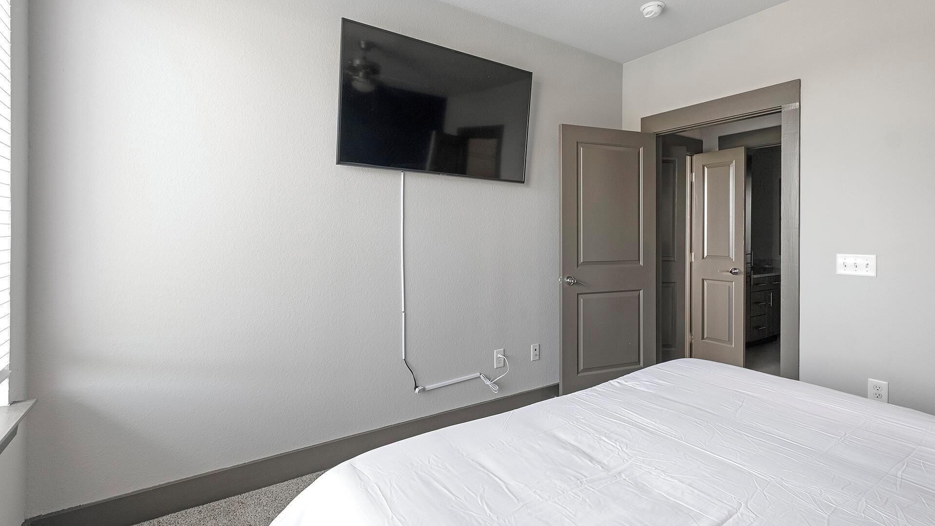Een hotelkamer met een bed, een aan de muur bevestigde televisie en een deur naar een badkamer.