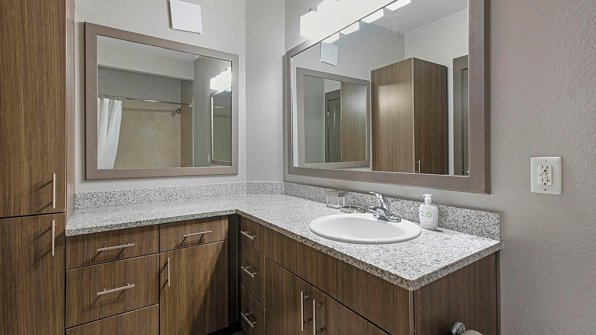 A bathroom with a granite countertop, a white sink, and wooden cabinets.