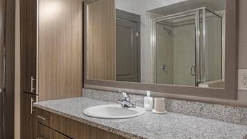 Un baño con encimera de granito, un lavabo blanco, un espejo y una ducha que se ve en el reflejo.
