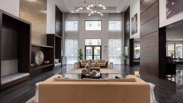 Eine geräumige Lobby mit einer zentralen Sitzecke, großen Fenstern und einem modernen Kronleuchter.