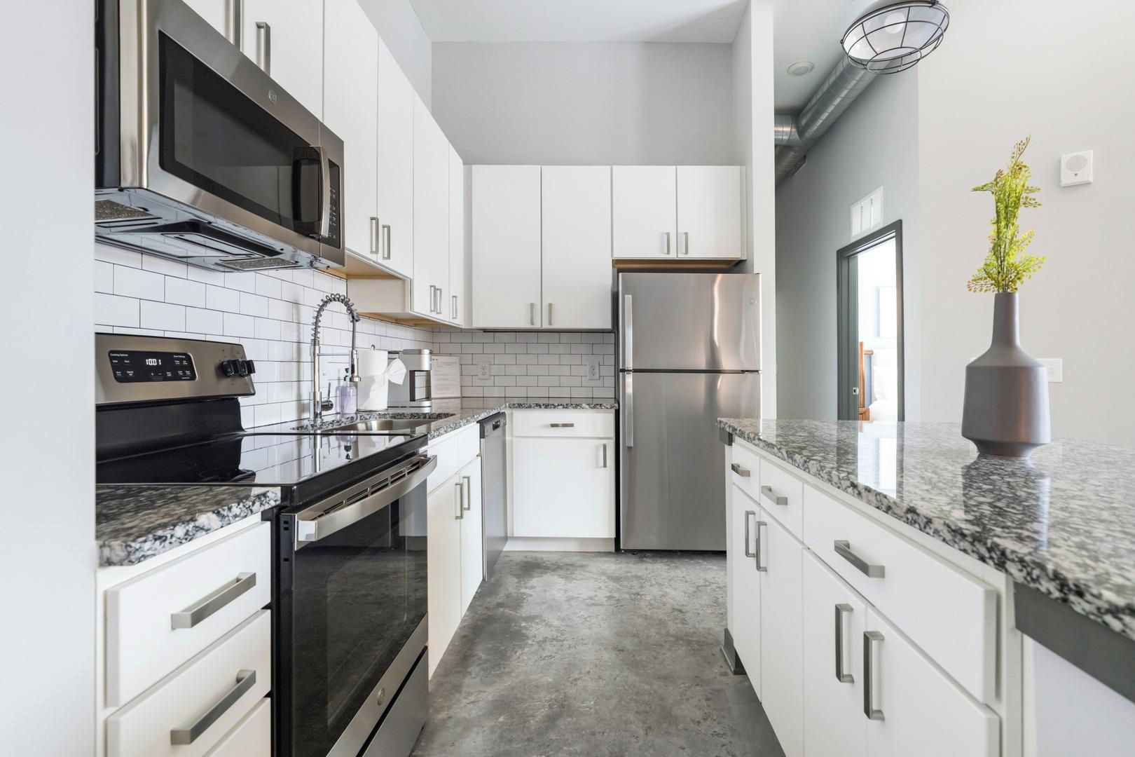 Una cucina moderna con elettrodomestici in acciaio inossidabile, mobili bianchi e un piano di lavoro in granito.