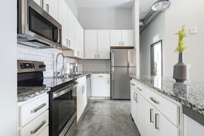 A modern kitchen with stainless steel appliances, white cabinetry, and a granite countertop. - Landing Apartments - Northwest Pensacola (Pensacola)